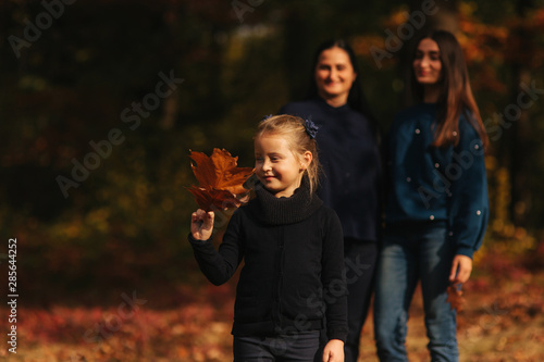 Little girl collect leaves in the forest. Background of mom dad and sister. Young family in autumn park