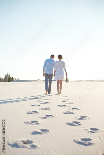 Happy couple walking holding hands at the beach