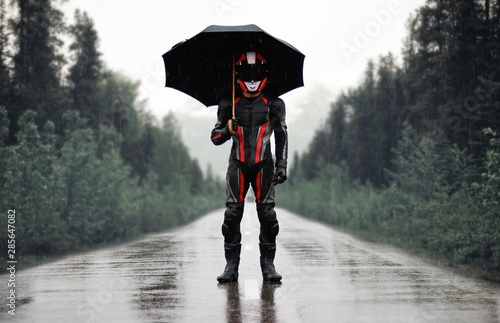 Motorcyclist in full gear and helmet with umbrella in the rain. Motorcyclist in the dark woods