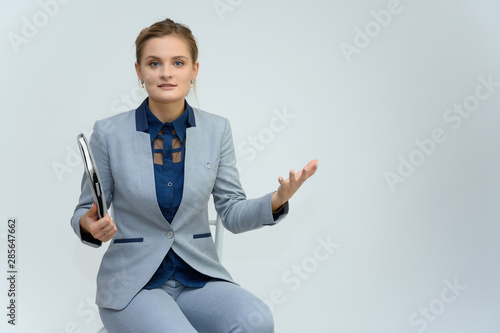 Wallpaper Mural Studio photo a waist-high portrait of a cute young woman girl in a business suit on a white background with a folder in hands. Sits in a chair right in front of the camera, explains, with emotions. Torontodigital.ca