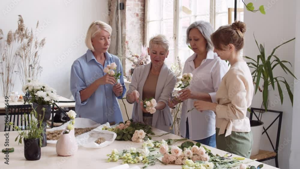 Pan shot of three Caucasian women standing at table in workshop and watching tutor showing how to cut roses using secateurs Pan shot of three Caucasian women standing at table in workshop and watching tutor showing how to cut roses using secateurs