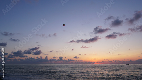Parasailing in blue sea during orange evening sundown on horizon, beautiful scenery of tranquil seascape in summer evening twilights. Tourists on a parachute over the sea. Sunset paradise  © Jimmy Tudeschi