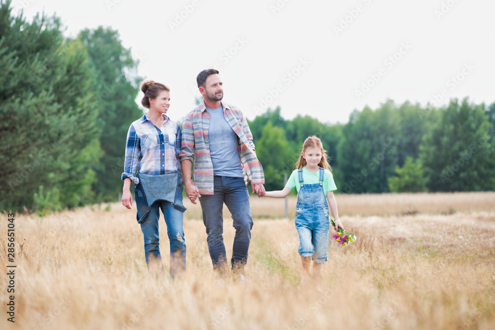 Young Caucasian family walking across field with young girl holding bouquet of flowers, concept organic ecologically friendly family Young Caucasian family walking across field with young girl holding bouquet of flowers, concept organic ecologically friendly family