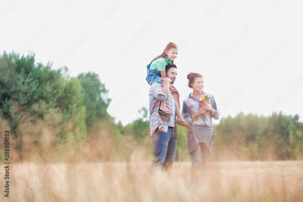 Young Caucasian family walking across field with young child on her fathers shoulders with the wife holding a bouquet of flowers