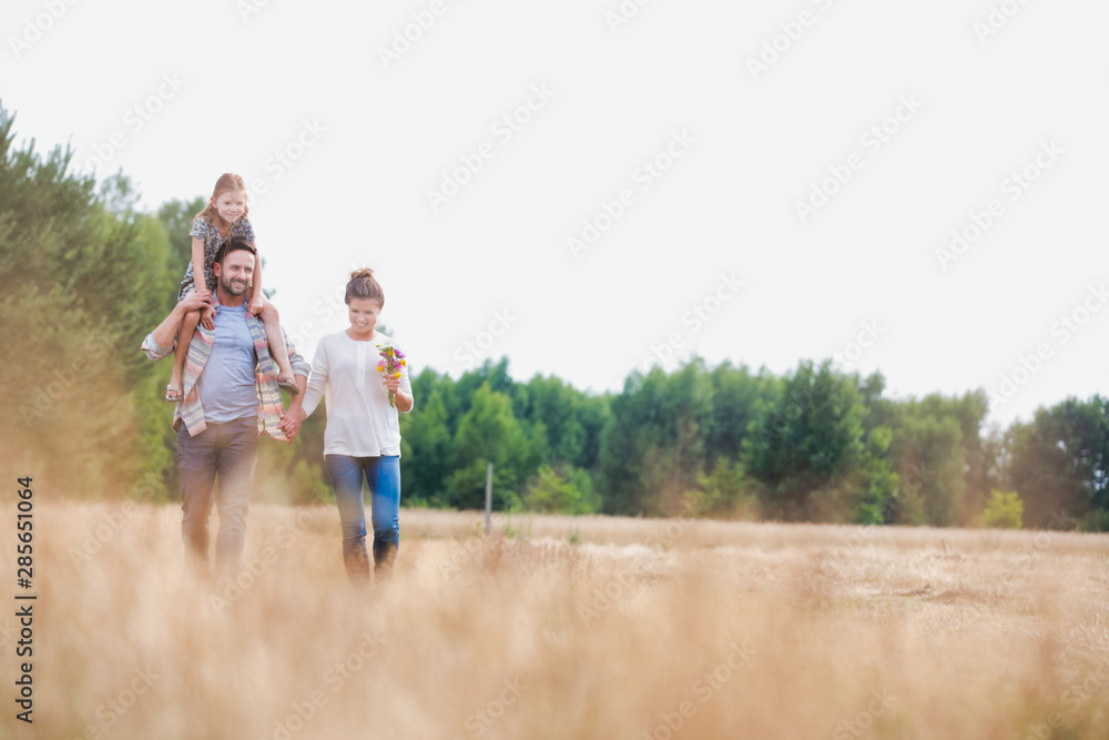 Young Caucasian family walking across field with young child on her fathers shoulders with the wife holding a bouquet of flowers Young Caucasian family walking across field with young child on her fathers shoulders with the wife holding a bouquet of flowers