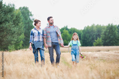 Young Caucasian family walking across field with young girl holding bouquet of flowers, concept organic ecologically friendly family