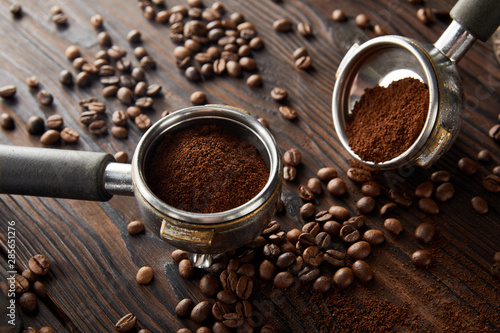 Portafilters with aromatic fresh coffee on dark wooden surface with coffee beans