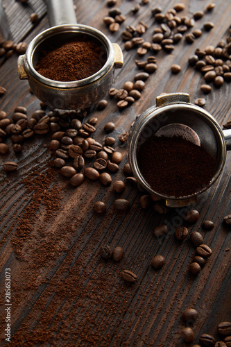 Portafilters filled with aromatic ground coffee on dark wooden surface with coffee beans