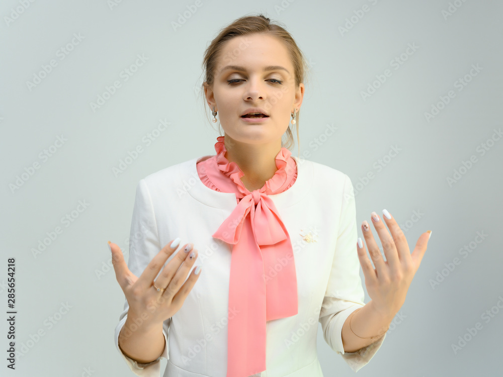 Photo studio portrait of a cute young woman girl in a beautiful suit of white-pink tender color on a white background. He stands right in front of the camera, explains with emotion. Photo studio portrait of a cute young woman girl in a beautiful suit of white-pink tender color on a white background. He stands right in front of the camera, explains with emotion.
