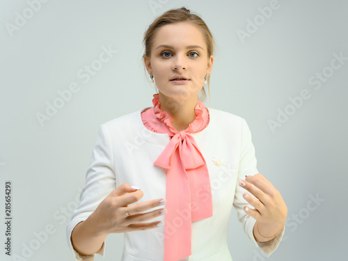 Photo studio portrait of a cute young woman girl in a beautiful suit of white-pink tender color on a white background. He stands right in front of the camera, explains with emotion. © Вячеслав Чичаев