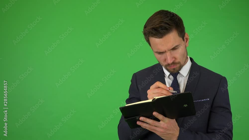 A young handsome businessman writes into a notebook - green screen studio A young handsome businessman writes into a notebook - green screen studio