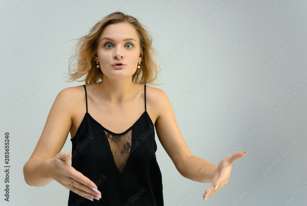 Photo studio portrait of a cute blonde young woman girl in a black blouse on a white background. He stands right in front of the camera, explains with emotion. Photo studio portrait of a cute blonde young woman girl in a black blouse on a white background. He stands right in front of the camera, explains with emotion.