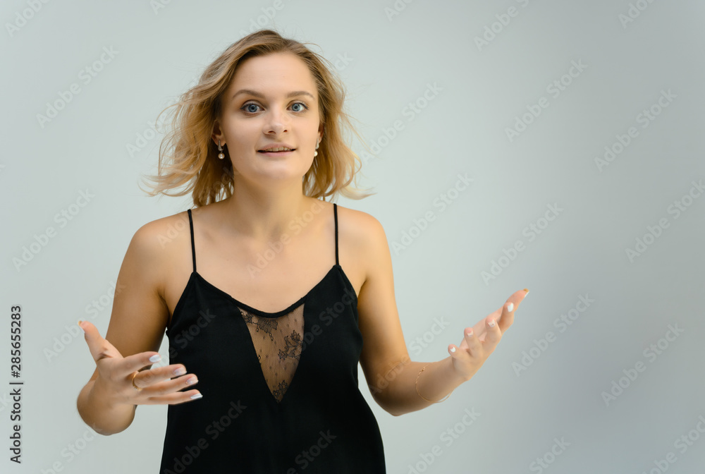 Photo studio portrait of a cute blonde young woman girl in a black blouse on a white background. He stands right in front of the camera, explains with emotion. Photo studio portrait of a cute blonde young woman girl in a black blouse on a white background. He stands right in front of the camera, explains with emotion.