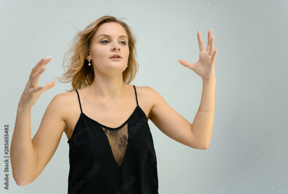Fototapeta premium Photo studio portrait of a cute blonde young woman girl in a black blouse on a white background. He stands right in front of the camera, explains with emotion.