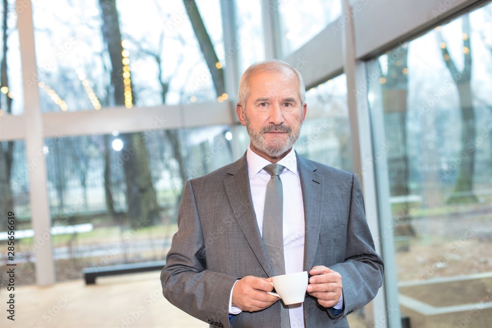 Confident businessman standing while drinking coffee in office Confident businessman standing while drinking coffee in office