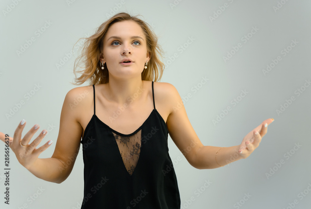 Photo studio portrait of a cute blonde young woman girl in a black blouse on a white background. He stands right in front of the camera, explains with emotion. Photo studio portrait of a cute blonde young woman girl in a black blouse on a white background. He stands right in front of the camera, explains with emotion.