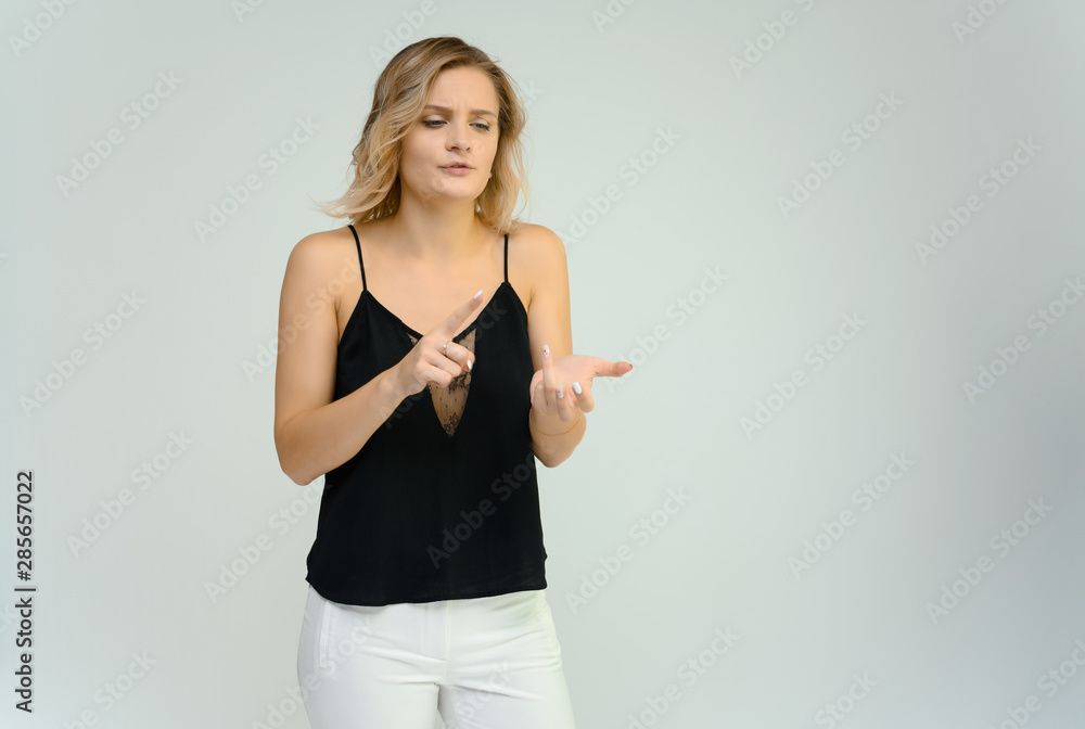 Photo studio portrait of a cute blonde young woman girl in a black blouse and white pants on a white background. He stands right in front of the camera, explains with emotion. Photo studio portrait of a cute blonde young woman girl in a black blouse and white pants on a white background. He stands right in front of the camera, explains with emotion.