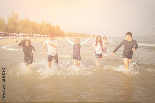 Women and men are running on the beach in the summer. Asian people are playing in the sea in Phetchaburi province, Thailand. Travel with friends concept.