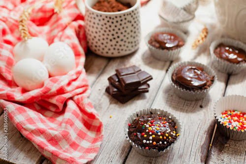 Сhocolate muffins with colorful pastry topping on a wooden table with ingredients
