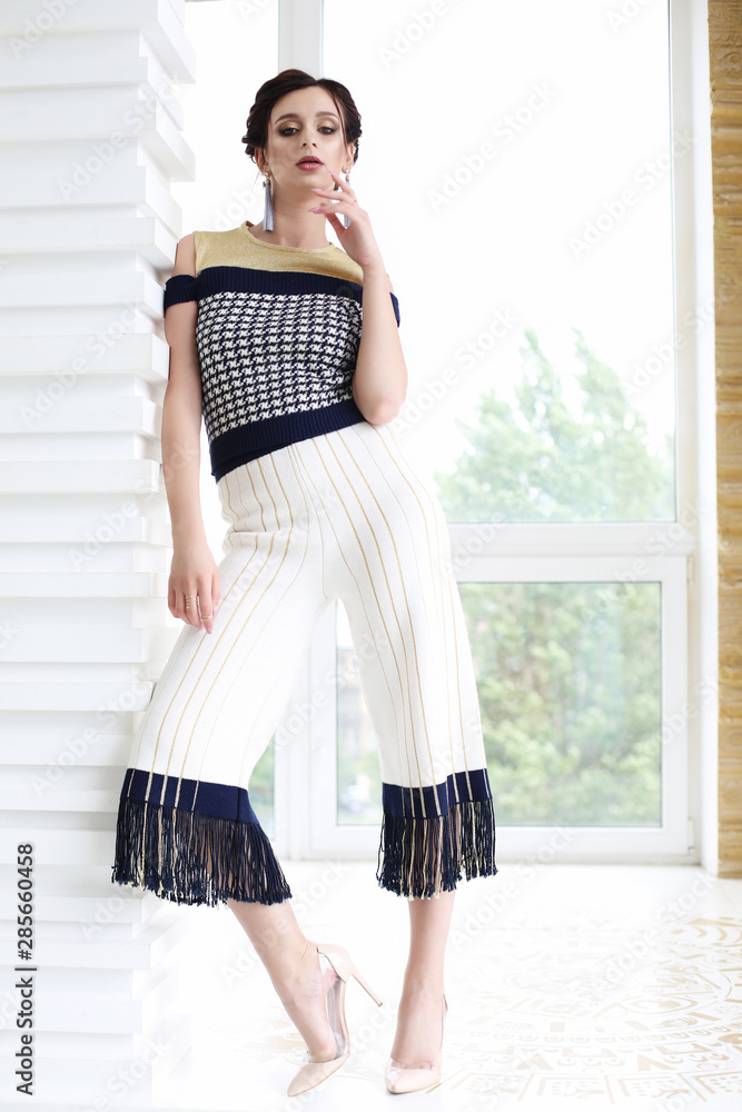 Young beautiful stylish woman dressed in white pants and top posing, fashionable style. Young beautiful stylish woman dressed in white pants and top posing, fashionable style.
