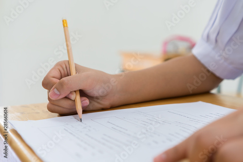 student taking notes lecture in high school or university with holding pencil writing on paperwork sheet and taking final exam in examination classroom