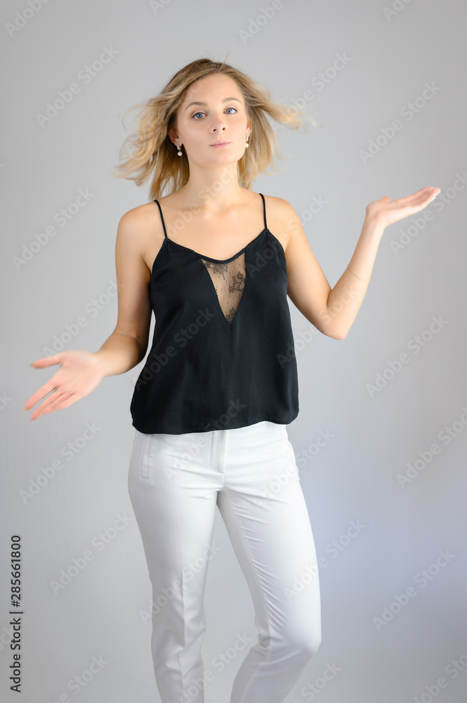 Full length studio portrait photo of a cute young blonde woman girl in a black blouse and white pants on a white background. He stands right in front of the camera, explains with emotion. Full length studio portrait photo of a cute young blonde woman girl in a black blouse and white pants on a white background. He stands right in front of the camera, explains with emotion.