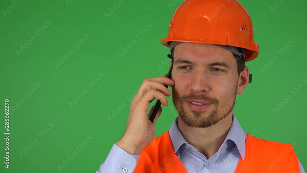 A young handsome construction worker talks on a smartphone with a mild smile - closeup - green screen studio A young handsome construction worker talks on a smartphone with a mild smile - closeup - green screen studio
