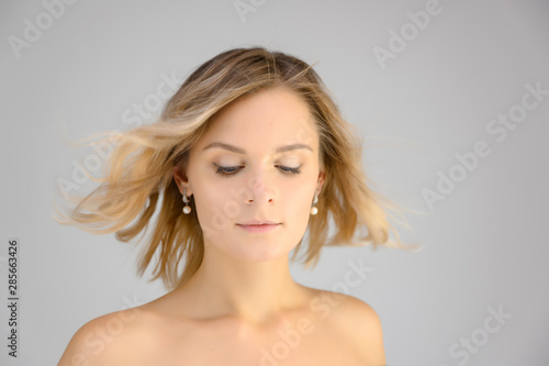 Closeup photo studio portrait of a fashionable pretty blonde young woman girl with beautiful hair on a white background. Standing right in front of the camera. Beauty, cosmetics.