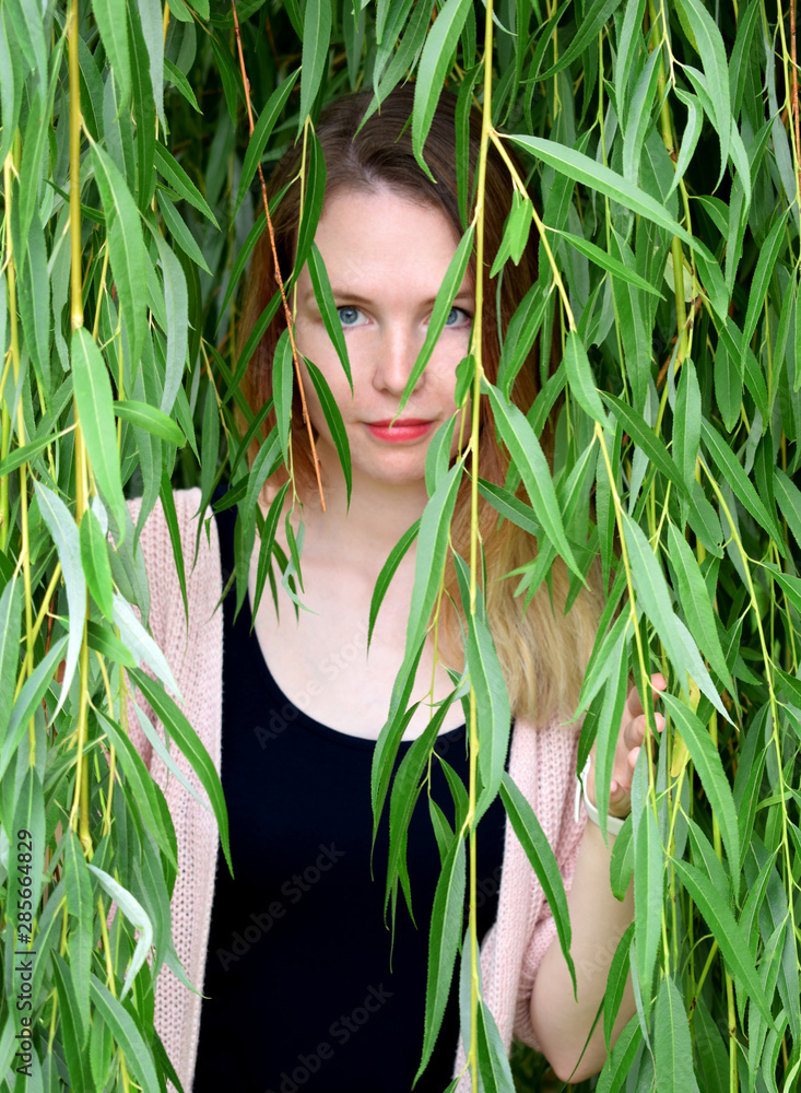 Portrait of young beautiful woman with natural make-up looking from behind green willow branches Portrait of young beautiful woman with natural make-up looking from behind green willow branches