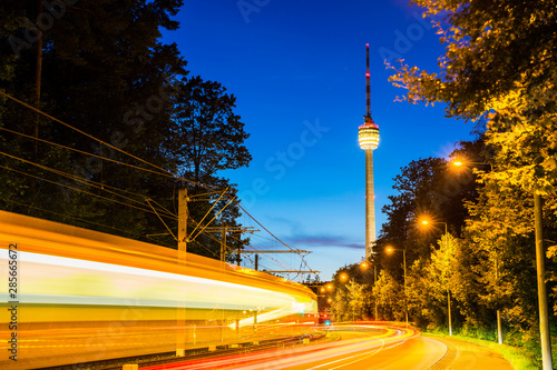 Germany, Stuttgart television tower and tramway illuminated by night at road with traffic and starry sky in summer surrounded by forest nature landscape