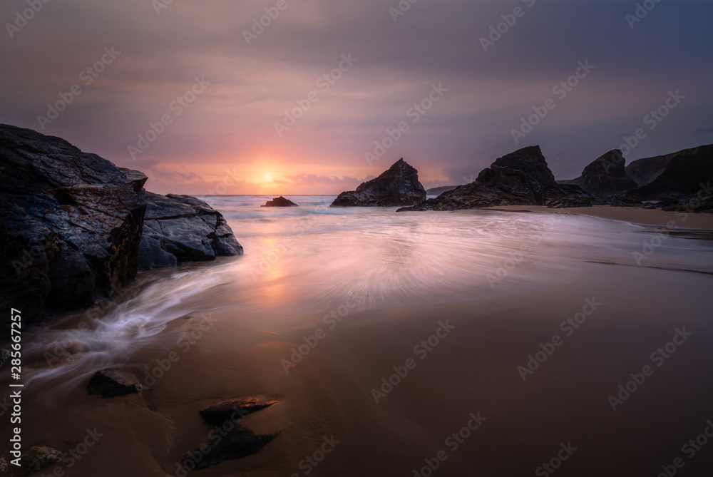 Sunset at the beautiful Bedruthan Steps in North Cornwall, with Silhouetted Sea Stacks, and Surf over Beach.