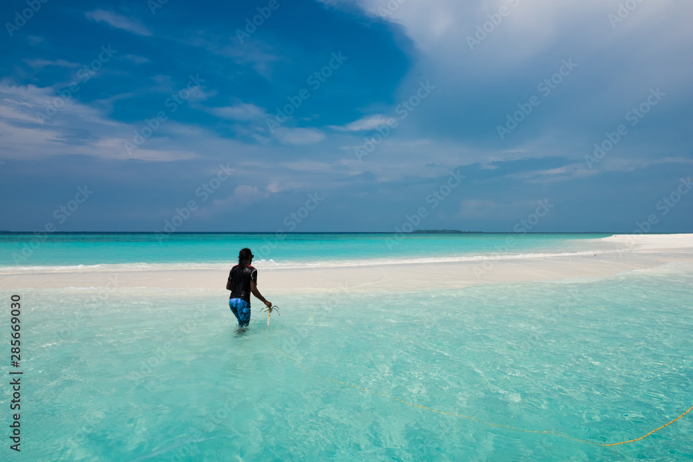 Man plants an anchor on a beach in the Maldives