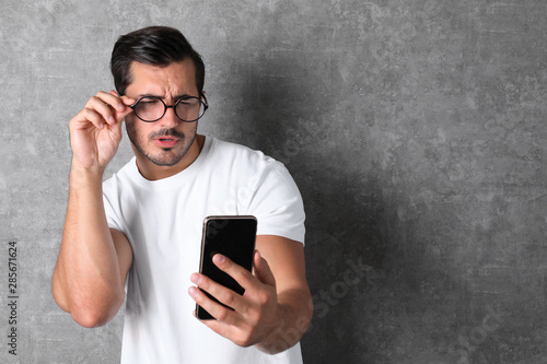 Young man with glasses using mobile phone on grey background, space for text. Vision problem photo