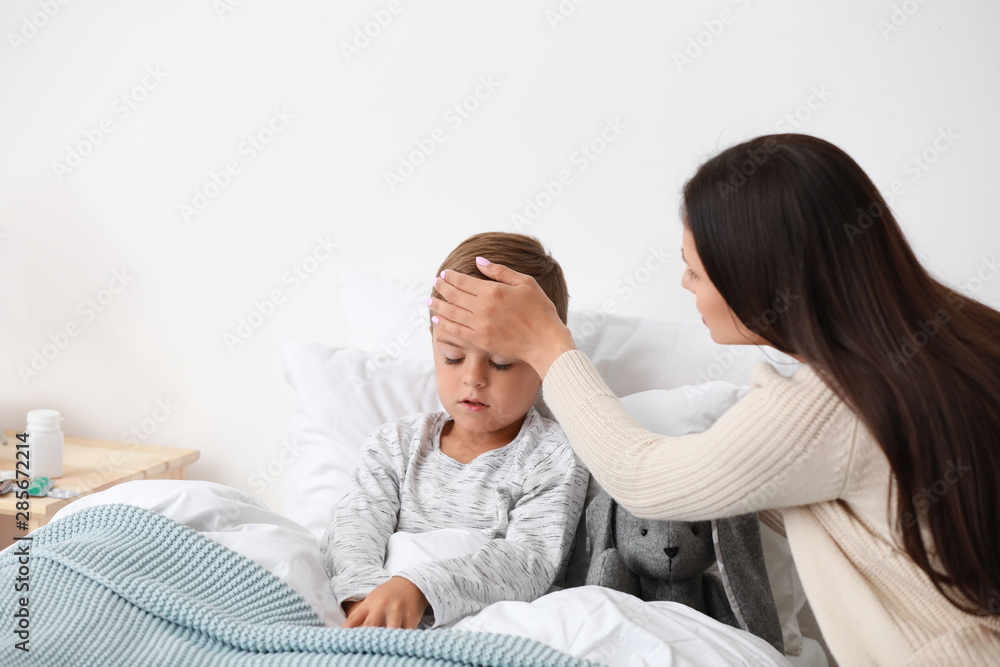 Mother taking care of her little son suffering from cold in bed, space for text Mother taking care of her little son suffering from cold in bed, space for text