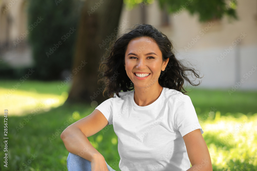 Happy young woman sitting on green grass in park on sunny day Happy young woman sitting on green grass in park on sunny day