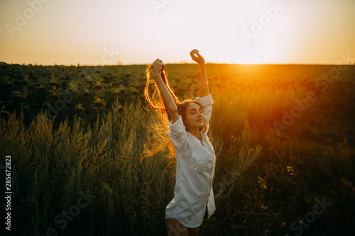 Happy joyful woman is walking on meadow at sunset.
