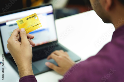 Hand holding credit card, typing on the keyboard of laptop, online shopping and electronic payments concept. 