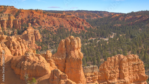 AERIAL: Flying over red rocky cliffs revealing car entering Bryce Canyon NP Utah