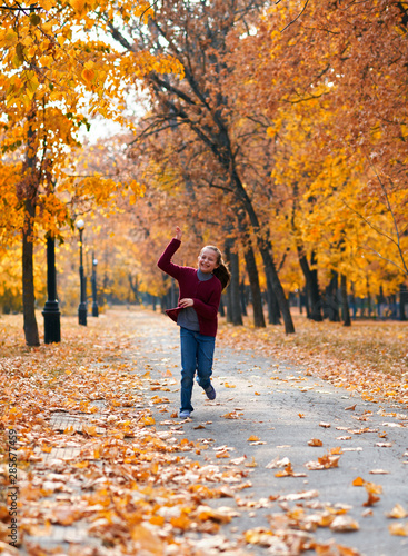 Happy child girl running, playing, posing, smiling and having fun in autumn city park. Bright yellow trees and leaves