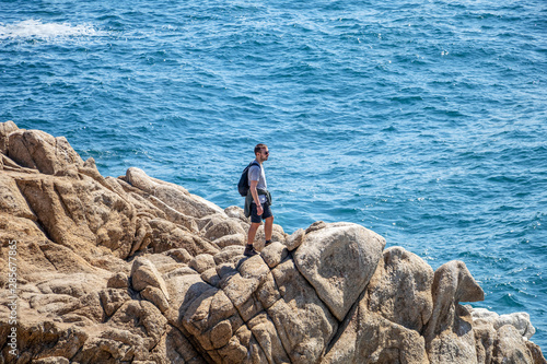 Young male traveler at rock formation rising out of cold Pacific ocean waters