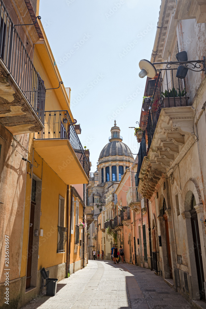 An alleyway of the ancient city of Ragusa Ibla in Sicily, Italy. In the background the dome of the cathedral.