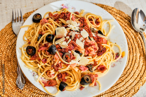 Spaghetti on plate with dried ham, tomatoes and olives