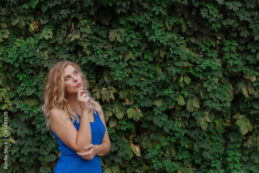 Young beautiful girl on a background of a wall of wild grapes, ponders, thinks an idea. Copy space. Young beautiful girl on a background of a wall of wild grapes, ponders, thinks an idea. Copy space.