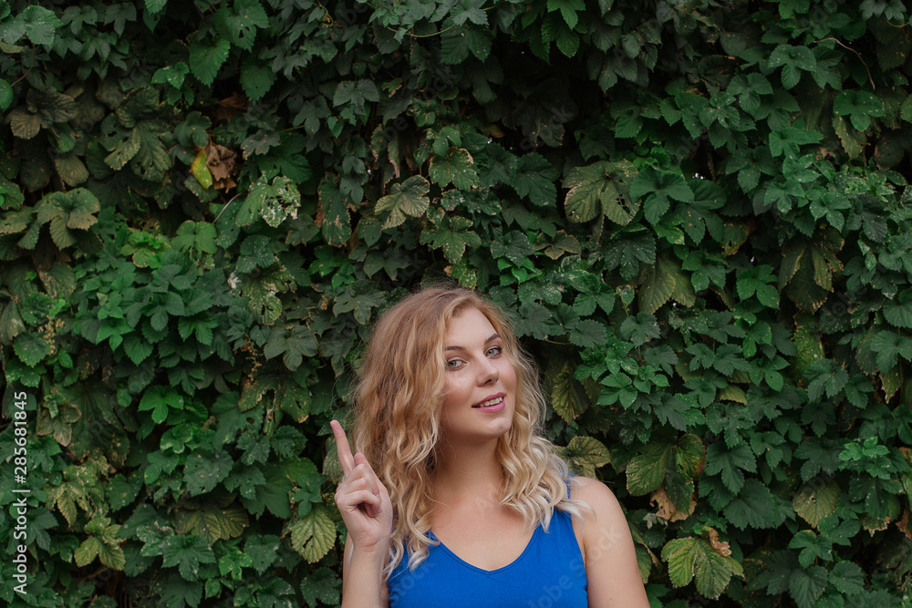 Young beautiful girl on a background of a wall of wild grapes, ponders, thinks an idea. Copy space. Young beautiful girl on a background of a wall of wild grapes, ponders, thinks an idea. Copy space.