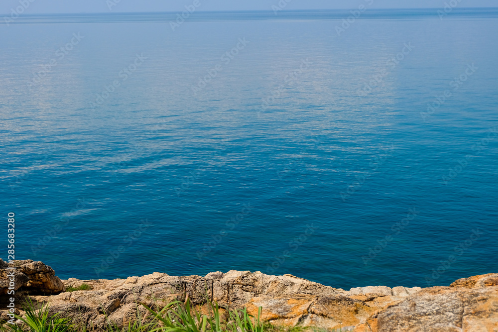 sea horizon with rocky shore cliffs and sun light blue sky background. Sea waves crashing on rocks, Samed, Thailand