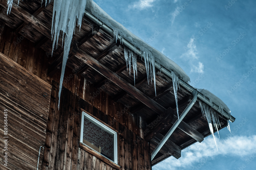 Wooden mountain chalet with icicles in Austrian Alps. Blue sky with clouds background