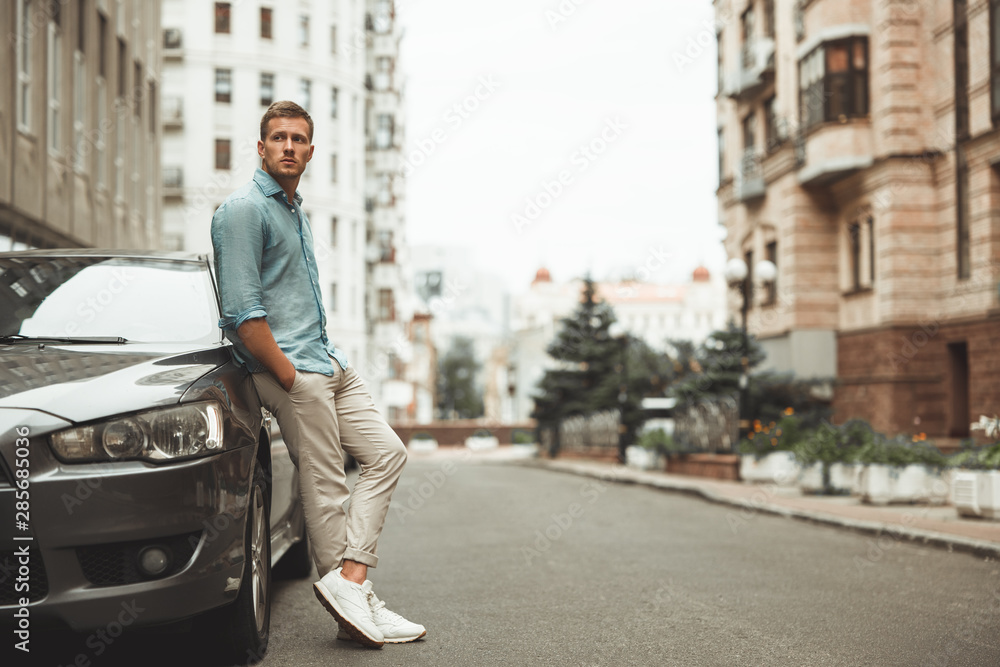 young handsome man standing near his parked car young handsome man standing near his parked car