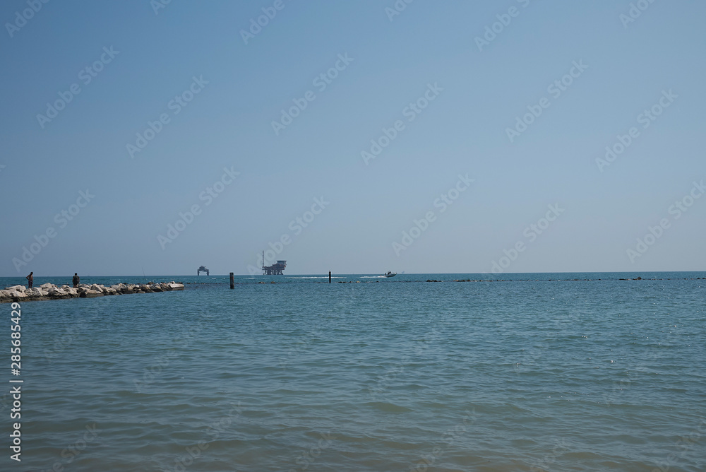 Lido di Dante, August 06, 2019 : View of Lido di Dante stone pier and platforms for the extraction of oil and natural gas in Adriatic sea in the backgroung