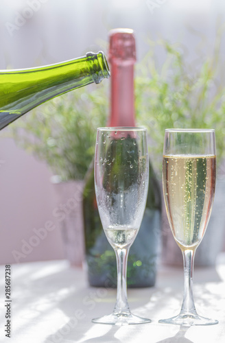 Close-up of a full champagne glass and an empty one, two green champagne bottles in the background. Concept of wedding.