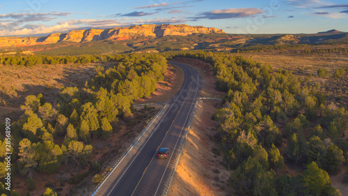 AERIAL: Black SUV car traveling towards mesa mountains in sunny Utah landscape